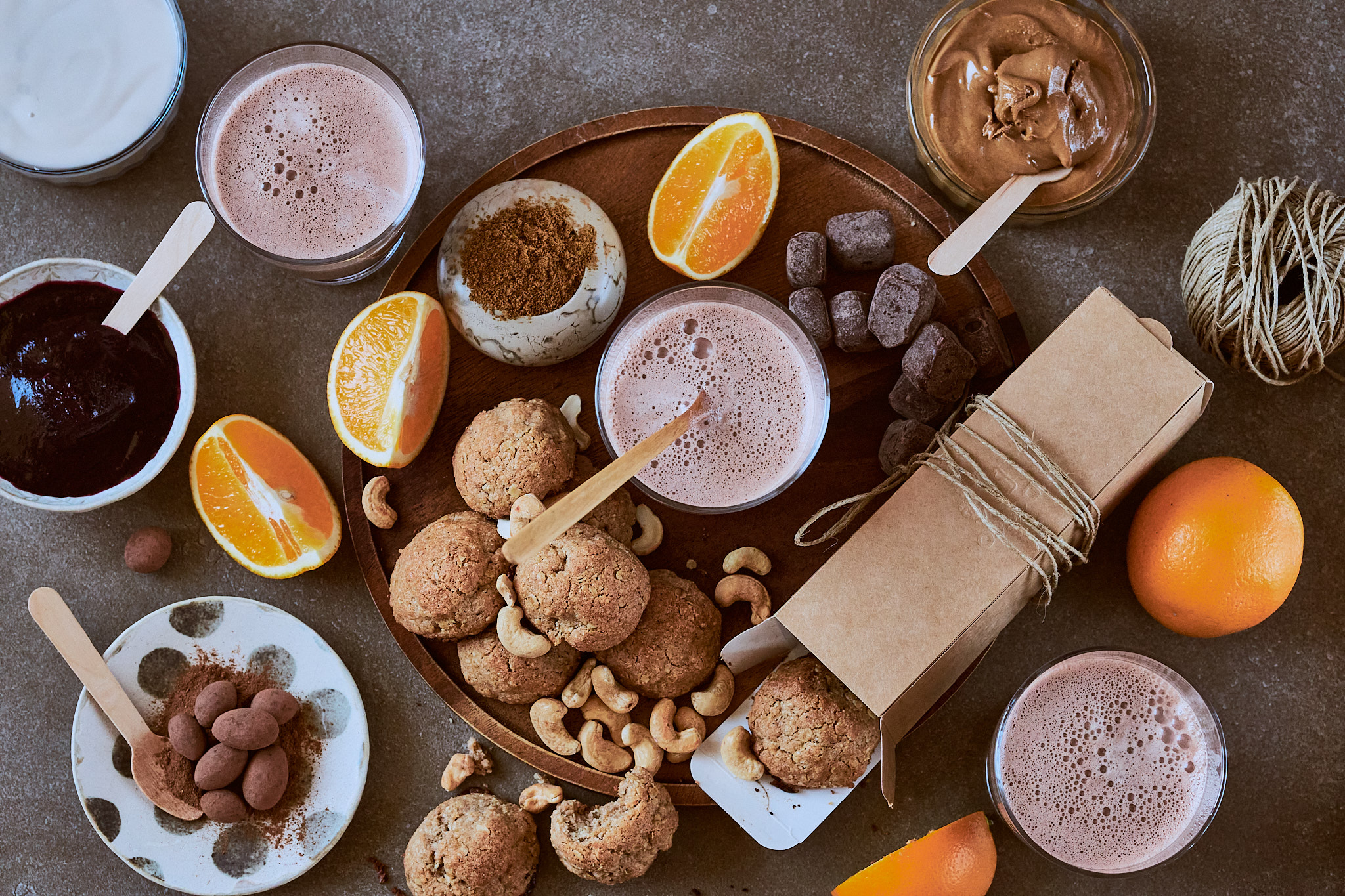 Assorted healthy treats, including chocolate drinks, cookies, fruit, and a gift box, displayed on a dark surface.